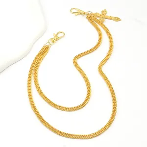 Detail of gold double chain trouser accessory featuring a cross pendant and lobster clasp