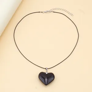 Detail of a minimalist black heart pendant with smooth finish and adjustable wax cord
