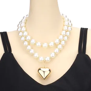 Double-layered pearl necklace with a large golden heart pendant on a model wearing black