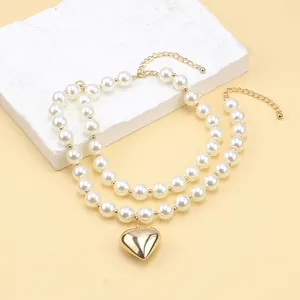 Detail view of double-layered pearl necklace with a polished gold heart pendant and lobster clasp