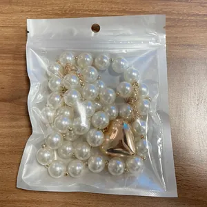 Detail of a white pearl necklace with a large golden heart pendant in clear packaging
