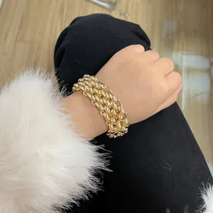 Detail eines mehrlagigen goldenen Gliederkettenarmbands am Handgelenk mit weißem Ärmel