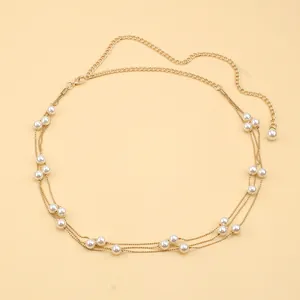 Detail of elegant multilayer gold waist chain with glossy white pearls on orange background