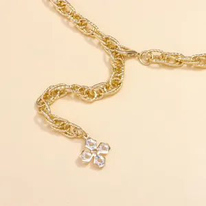 Detail of gold metal waist chain featuring textured links and a clear floral crystal charm