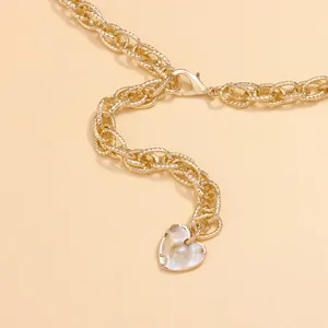 Macro view of gold chain belt featuring a textured metal link and iridescent heart pendant