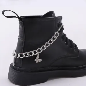 Dettaglio dello stivale nero in pelle con catena d'argento e ciondolo a farfalla di strass