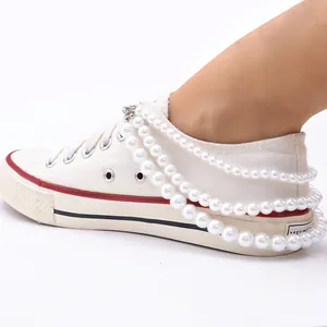 Detail von mehrlagigen weißen Perlen-Schuhketten mit Metallschließen an Turnschuhen