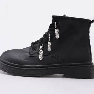 Detalle de botas de cuero negro con cordones y creativos colgantes metálicos de zapatos plateados