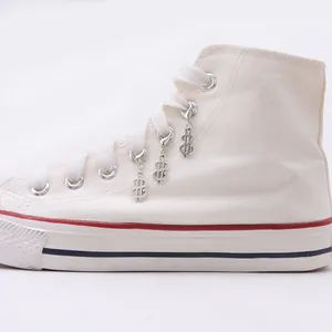 Three silver dollar sign charms with lobster clasps attached to white canvas sneakers