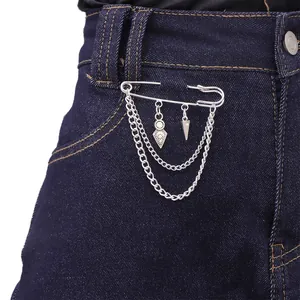 Silver safety pin brooch with hanging metal chains and geometric pendants on denim fabric