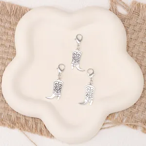 Three vintage silver cowboy boot charms with lobster clasps on a decorative petal plate