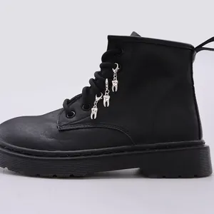 Detalle de botas de plataforma negras con colgantes metálicos únicos en forma de diente