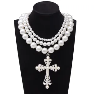 Dettaglio di una collana di perle multistrato con grande ciondolo a croce argentata