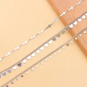 Silver metal accessory chain with cross, heart, and star pendants on wooden blocks