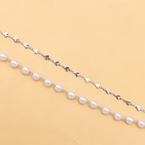 Dettaglio di una catena con cuori argentati e una tracolla di perle su sfondo giallo