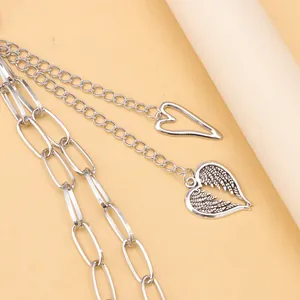 Détail d'une chaîne de pantalon multicouche en métal argenté avec pendentifs cœur et aile