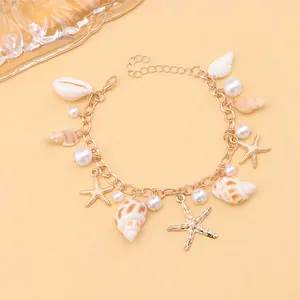 Detail of gold ocean bracelet with shells, pearls, and starfish charms on apricot backdrop