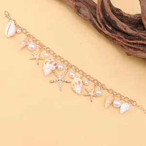 Detail of bohemian gold bracelet featuring seashell, starfish charms and faux pearls
