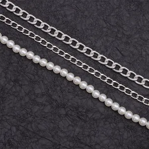 Detailed view of triple-layered silver metal chains and white pearls on black texture