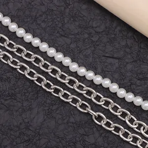 Detail of layered hip-hop waist chain with white pearls and silver metal links on dark background
