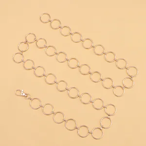 Detail view of the gold metal waist chain showing circular links and lobster clasp closure