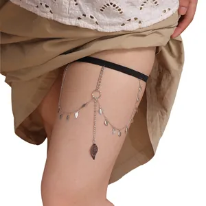 Close-up of bohemian leg chain with silver leaf pendants and black elastic band