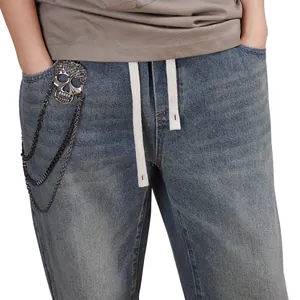 Detail of multi-layer metal skull waist chain on blue washed denim pants with drawstring