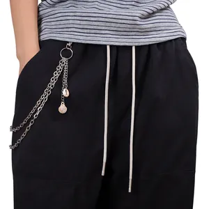 Détail de chaînes métalliques argentées avec pendentifs coquillages sur pantalon noir
