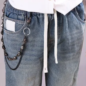Detalle de vaqueros azules con cadena de calavera negro mate y cintura elástica con cordón