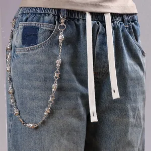 Punk silver trouser chain with skull charms and barbed wire links on blue denim