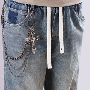 Detalle de cadena de pantalón multicapa con colgante de cruz de strass sobre vaqueros azul claro