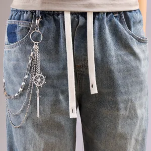 Detail of layered silver pants chain with steering wheel and sword pendant on denim