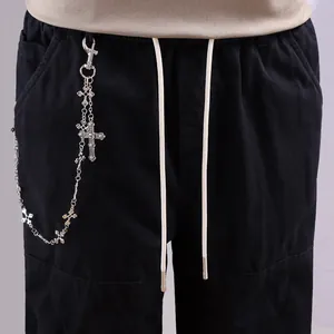 Détail de la chaîne à croix gothique argentée sur un pantalon cargo noir à cordons blancs