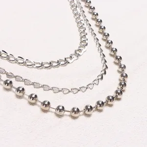 Detail view of multi-layer silver chains with curb, heart, and ball link patterns