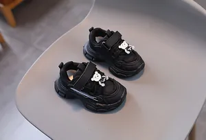 Détail de baskets noires pour enfants avec fermeture velcro et décoration d'ours en 3D