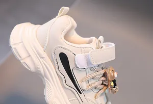 Détail latéral de baskets beiges pour enfants avec breloque ours et velcro