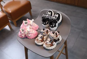 Three pairs of kids thick-sole sneakers in pink, black, and brown displayed on a chair