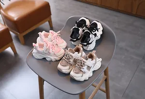 Three pairs of plush children's sneakers in pink, black, and beige on a grey chair
