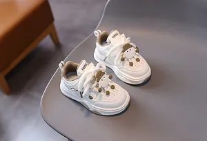Dettaglio di sneaker beige per bambini con lacci bianchi tondi e ciondolo mostro carino