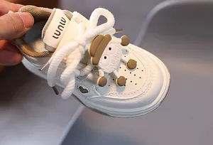 Dettaglio di scarpa sportiva per bambini in pelle bianca con cuori e ciondolo a cartone