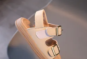 Close-up of beige kids' sandals featuring dual metal buckles and velcro closures