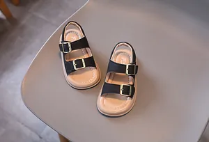 Detail of kids black double-strap sandals with golden buckles and soft beige soles