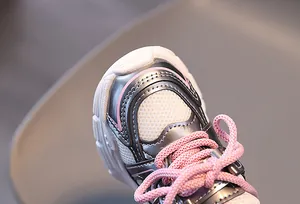 Détail de maille respirante et lacets roses sur baskets argentées pour enfant