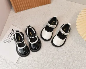 Detalle de merceditas de charol para niña con tiras de pedrería en color negro y crema