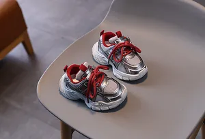Détail de baskets enfant en maille argentée avec de gros lacets rouges sur siège