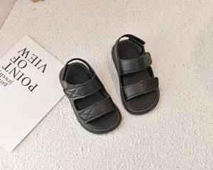 Vista dall'alto di sandali in pelle nera per bambini con cinturini con cuciture a X su tappeto