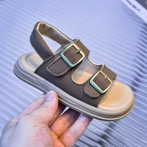 Detail of dark brown leather kids' sandals with gold buckles and white stitching