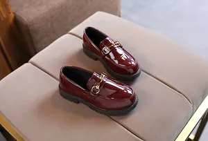 Close-up of wine red patent leather kids loafers with gold horsebit buckle and rubber sole