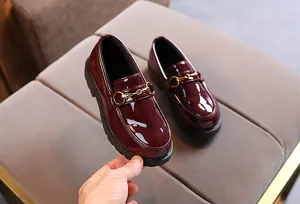 Close-up of burgundy patent leather kids loafers with elegant gold metal horsebit detail
