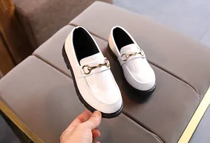 Detail of white patent leather kids loafer with gold horsebit and black thick sole